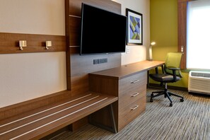Habitación de hotel con escritorio de madera, televisor de pantalla plana, banco, silla verde y una obra de arte enmarcada en la pared.