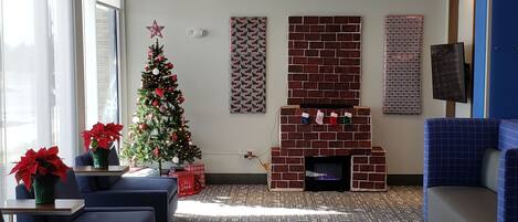 A modern lobby with a patterned carpet, seating area, Christmas tree, and a brick fireplace.