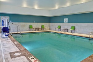 An indoor swimming pool with clear water, a no diving sign, and several green chairs along the poolside.