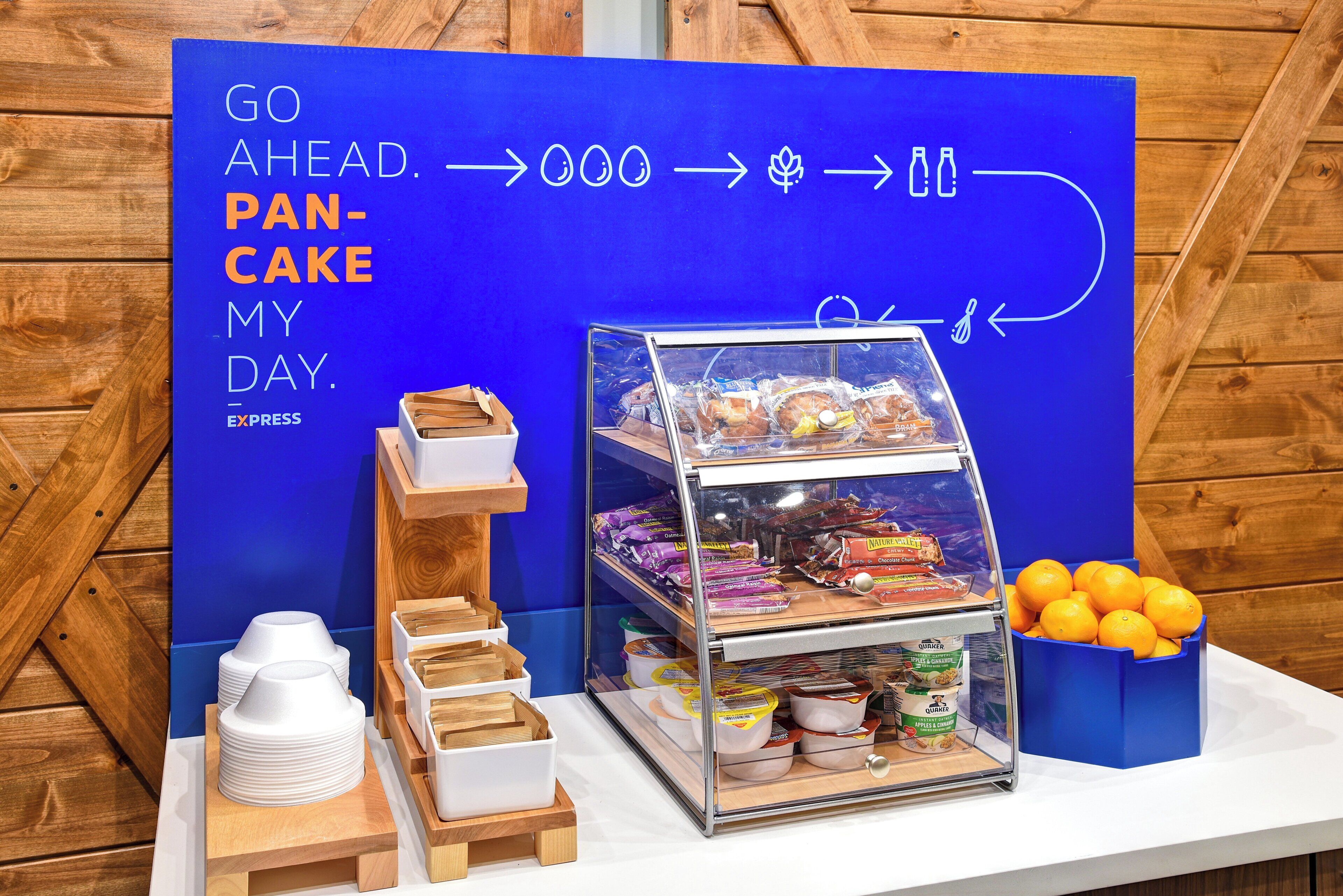 Un panneau bleu avec des flèches indiquant la direction et du texte, une vitrine contenant des produits emballés, une pile d’assiettes blanches et une boîte d’oranges.