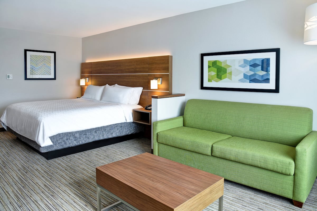A hotel room with a bed, a green sofa, and a wooden coffee table.