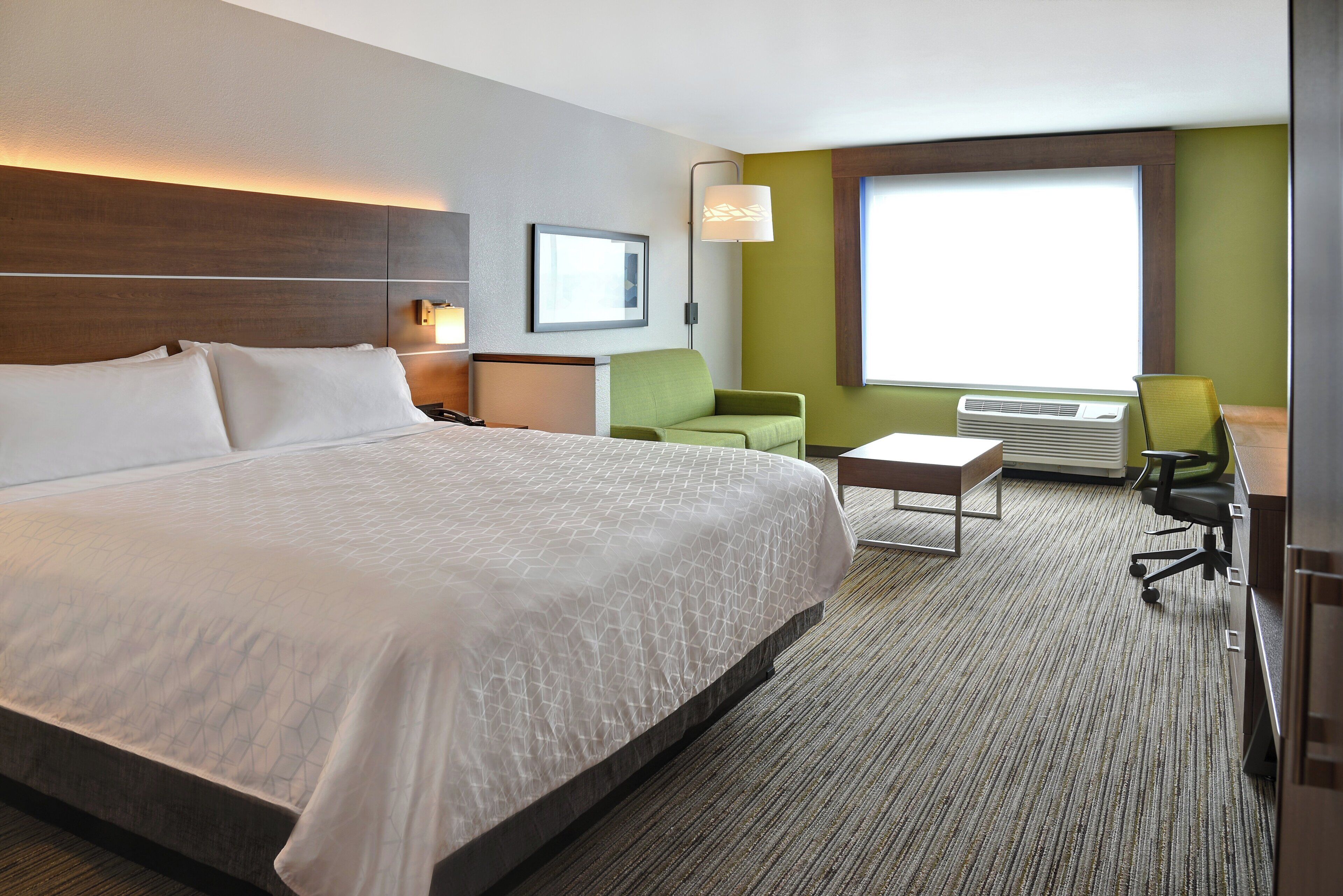 Habitación de hotel con una cama grande, un escritorio, una silla, una lámpara y una ventana.
