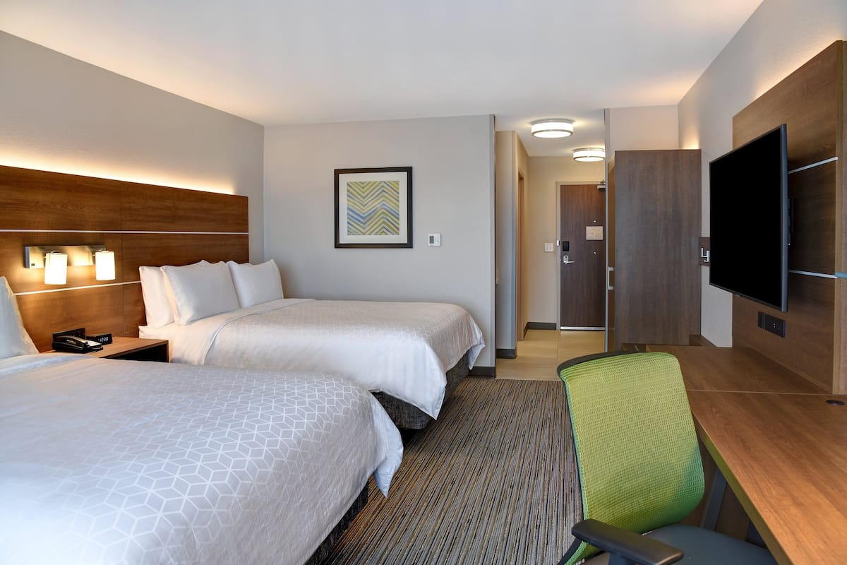 A hotel room with two beds, a desk, a chair, a television, and a framed picture on the wall.