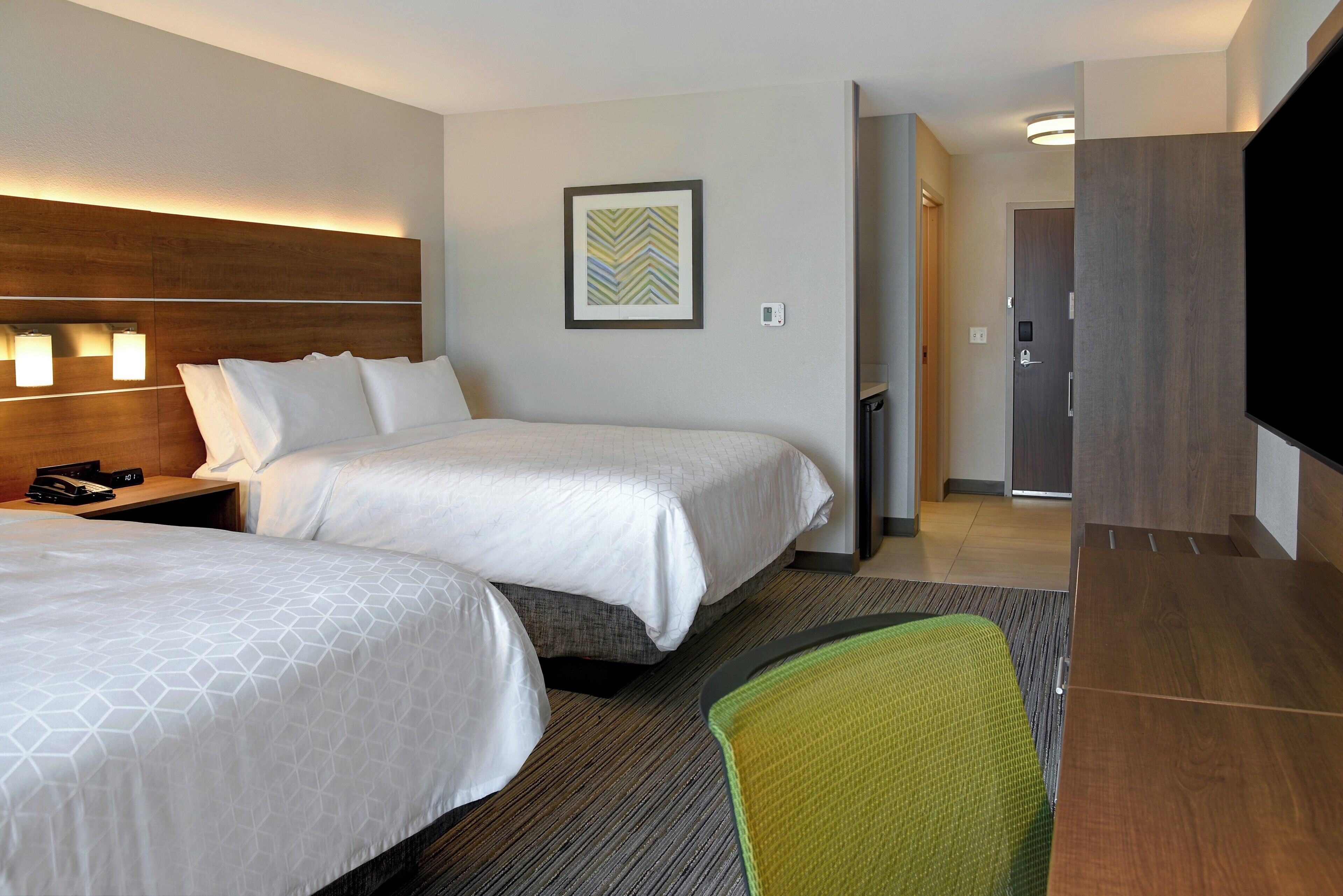 A hotel room with two beds, a desk with a telephone, a framed picture on the wall, and a television on the right.