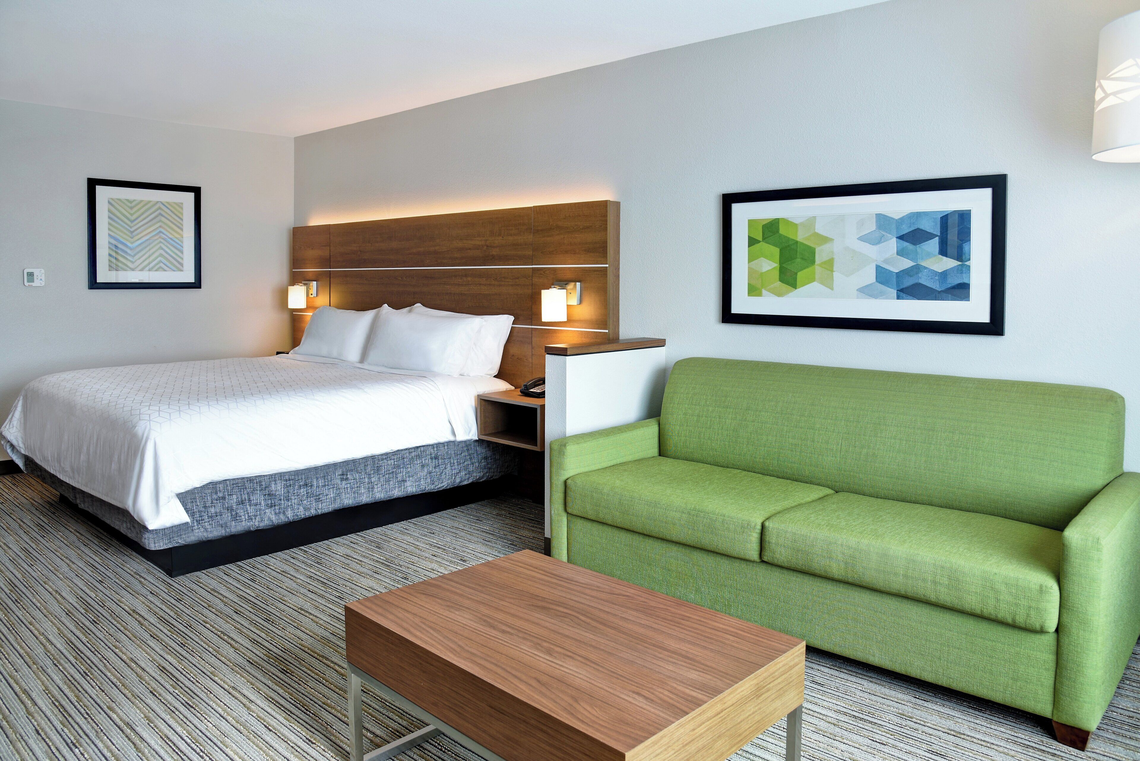 A hotel room with a bed, a green sofa, a wooden table, and two wall-mounted lamps.