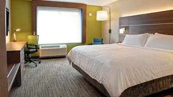 Quarto de hotel com uma cama grande, uma escrivaninha com cadeira, uma janela com persianas e uma luminária na parede.
