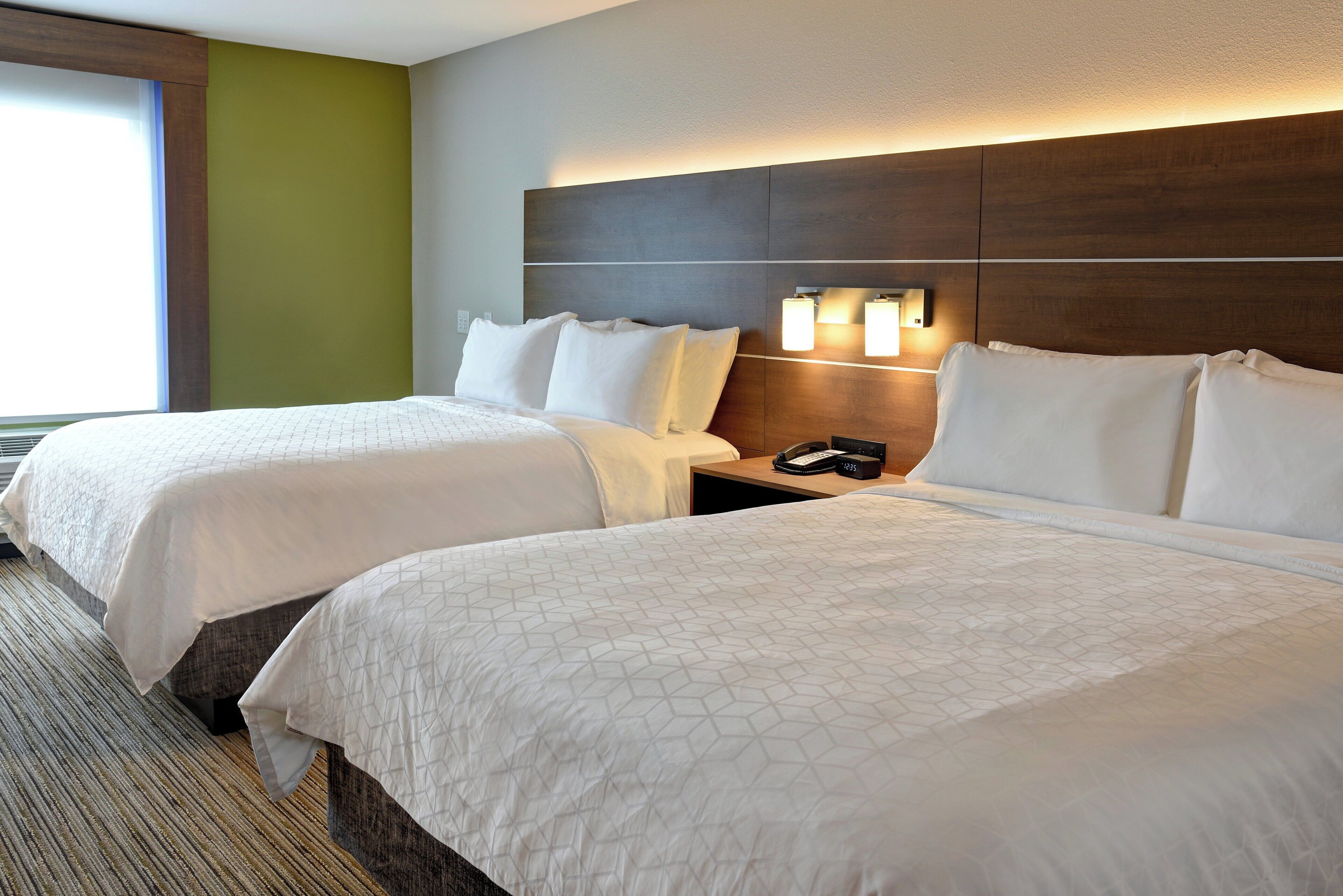 A hotel room with two beds, a nightstand, a phone, and a wall-mounted light fixture.