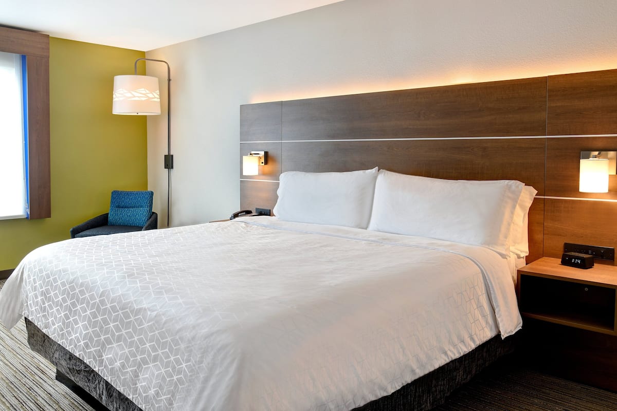 A hotel room with a large bed, a nightstand, a lamp, and a chair.
