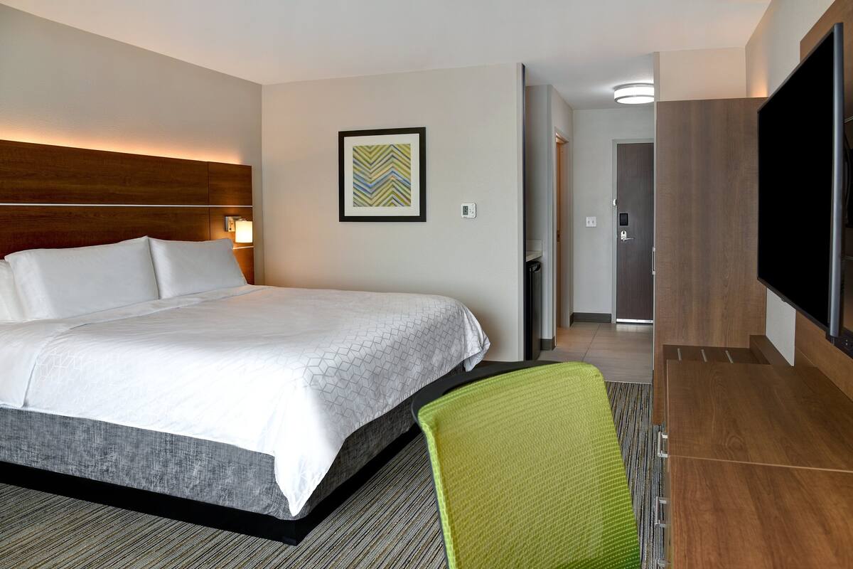 A hotel room with a large bed, a green chair, a flat-screen TV, and a framed picture on the wall.
