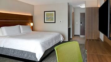 A hotel room with a large bed, a green chair, a flat-screen TV, and a framed picture on the wall.