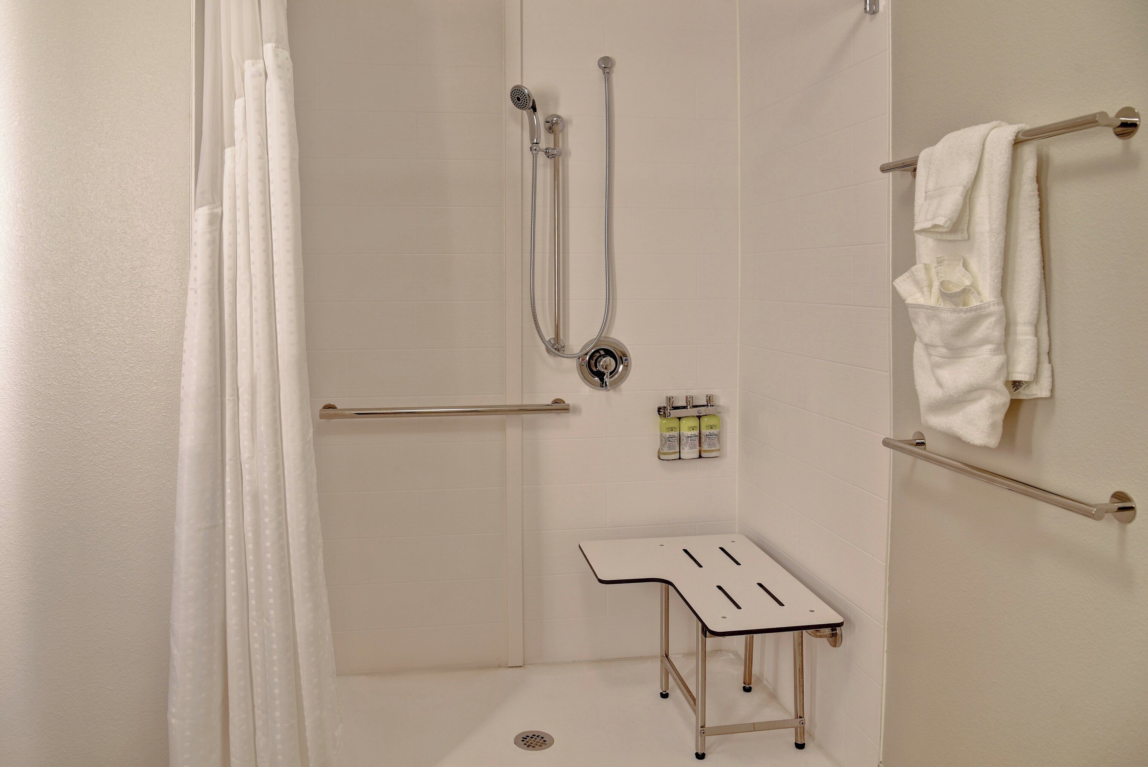 A shower area with a showerhead, handheld shower, and a small table with bottles.