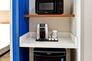Una kitchenette con microondas, cafetera y cápsulas de café sobre una encimera blanca.