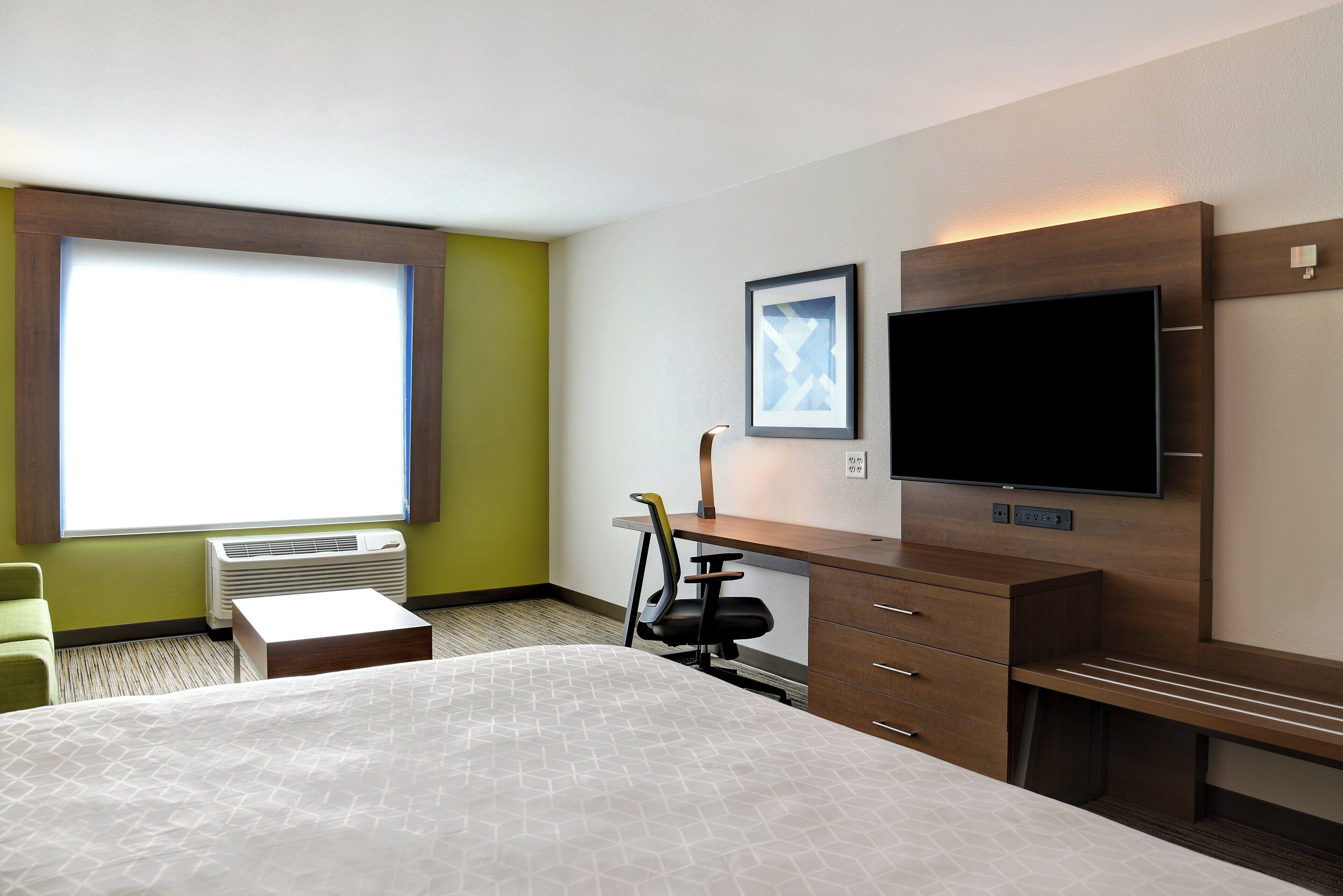 Una habitación de hotel con cama, escritorio, silla, televisor y ventana.