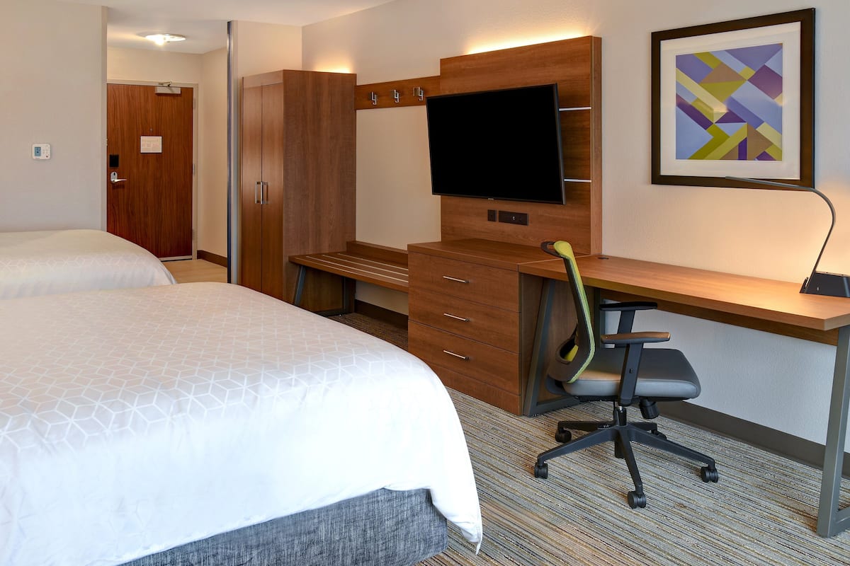 A hotel room with two beds, a desk, a chair, a TV, and a framed picture on the wall.