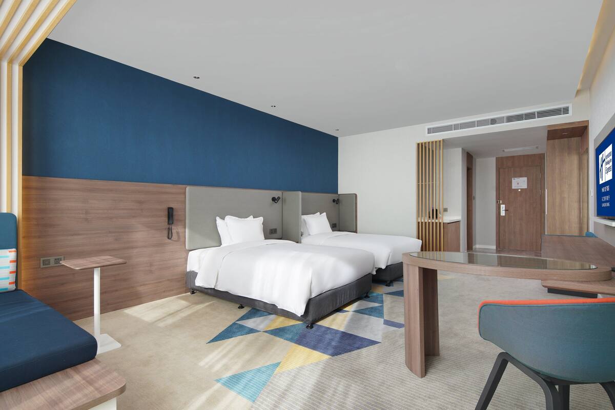 Ein Hotelzimmer mit zwei Betten, einem Schreibtisch, einem Stuhl und einem Spiegel.