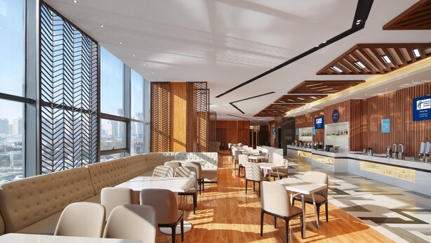 A modern hotel lobby with a long seating area, a reception desk, and large windows offering a city view. - Holiday Inn Express Ulanqab Jining by IHG (Ulaan Chab)
