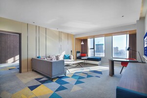 Quarto de hotel moderno com sofá, escrivaninha e vista para a cidade.