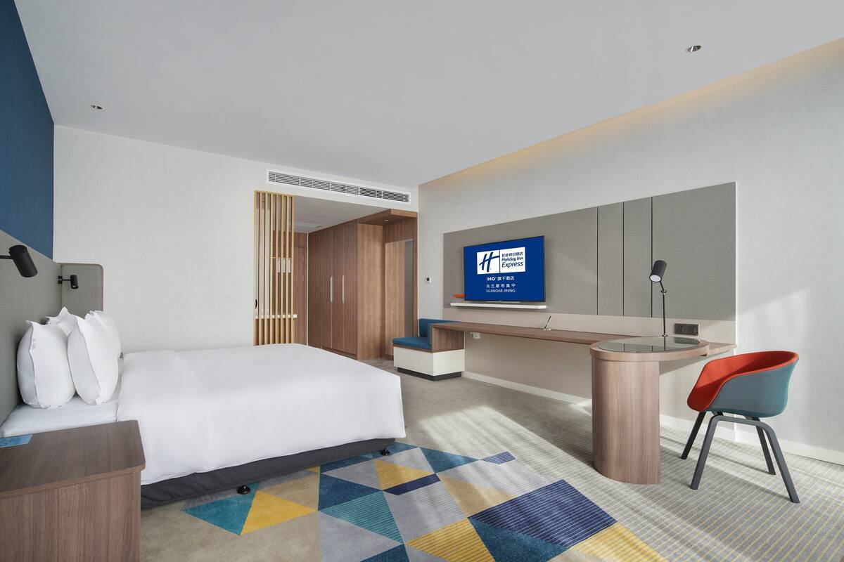 Ein modernes Hotelzimmer mit einem großen Bett, einem Schreibtisch, einem Fernseher und einem Sessel.