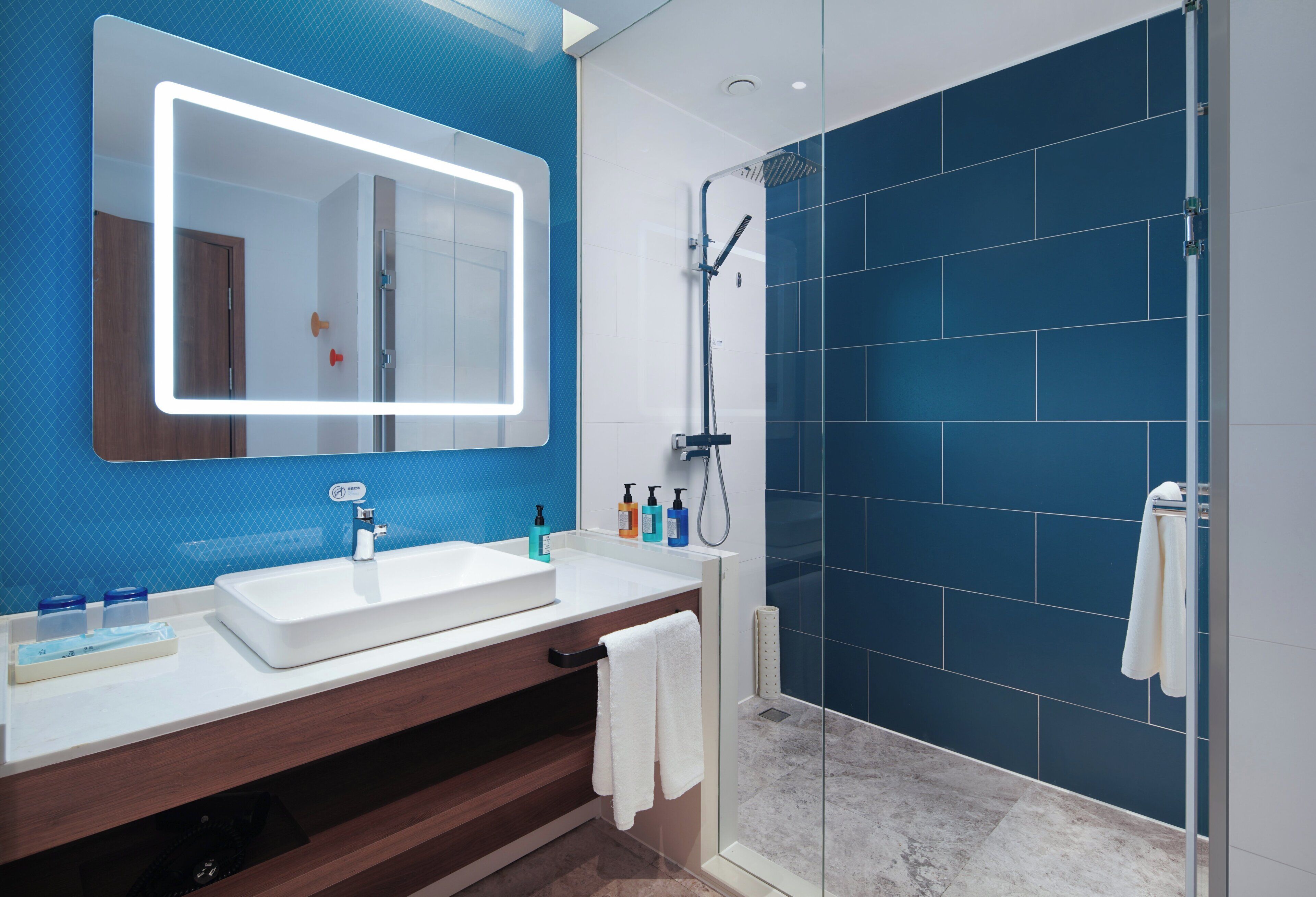 Un baño moderno con un espejo grande, un lavamanos blanco y una zona de ducha.