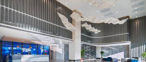 A spacious lobby with a reception desk, seating area, and a modern ceiling design.