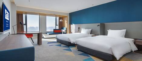 A hotel room with two beds, a desk, a chair, and a large window with a city view.
