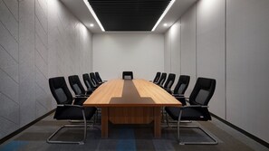 A conference room with a long wooden table surrounded by black chairs, a carpeted floor, and a ceiling with a linear light fixture.
