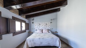 Ein Schlafzimmer mit einem Bett, Holzbalken, einem Fenster und einer Wandleuchte.