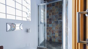 Ein Badezimmer mit Duschkabine aus Glas, weißen Fliesen und einem Fenster über dem Waschbecken.
