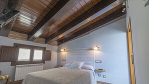 Ein Schlafzimmer mit einem großen Bett, Holzbalken an der Decke, einem Fenster und einer Heizung.