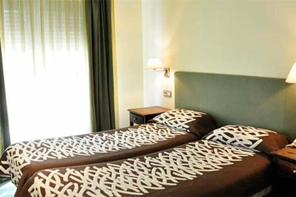 A hotel room with two beds, a nightstand, a lamp, and a window with curtains. - Tivoli (Andorra la Vella)