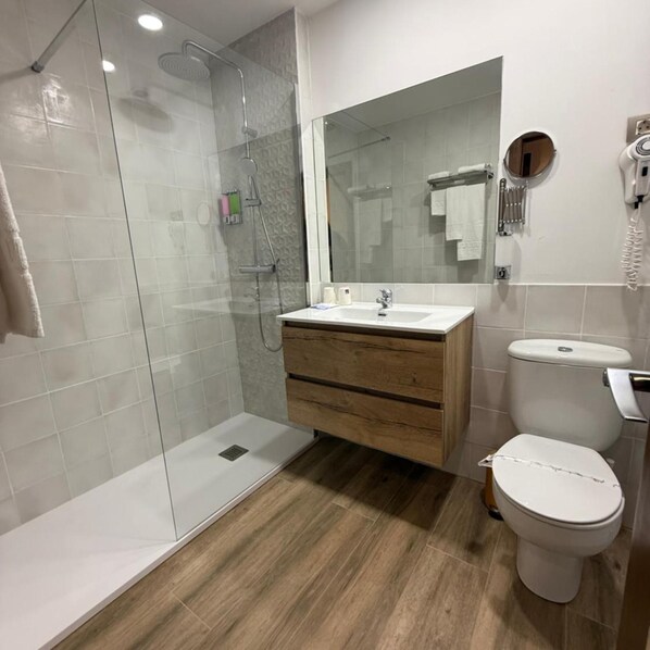 A modern bathroom with a glass shower enclosure, a wooden vanity, a white sink, and a toilet. - Tivoli (Andorra la Vella)
