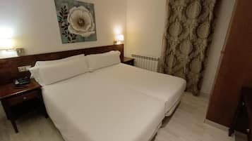 Habitación de hotel con una cama grande, una mesita de noche con teléfono, una lámpara de pared y un radiador.