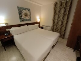 Habitación de hotel con una cama grande, una mesita de noche con teléfono, una lámpara de pared y un radiador.