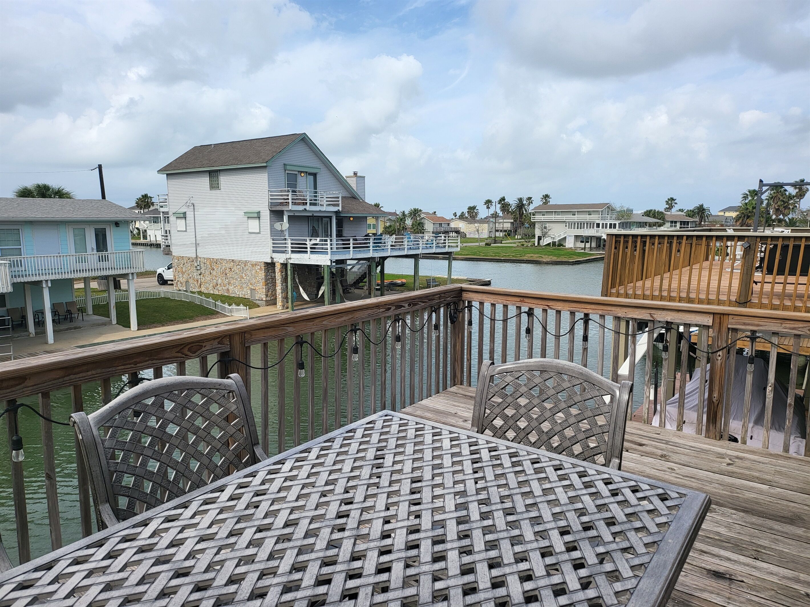 Une terrasse en bois avec une table et des chaises, donnant sur une étendue d’eau, avec des maisons et un quai en arrière-plan.