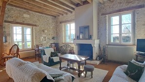 A rustic room with exposed stone walls, a fireplace, a television, and a cozy seating area with a table and chairs.