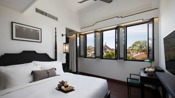 Habitación de hotel moderna con una cama grande, un escritorio y vistas a un edificio tradicional a través de amplios ventanales.