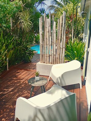A patio with a pool, surrounded by lush greenery and bamboo fencing. - Atemoya lodges. Swimming pool, beach 400 m., Cinnamon (4p), A/C, pool, beautiful garden, beach 400 m (Deshaies)