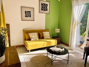 A yellow sofa with patterned cushions, a black coffee table, and framed artwork on the wall. - Atemoya lodges. Swimming pool, beach 400 m., Cinnamon (4p), A/C, pool, beautiful garden, beach 400 m (Deshaies)