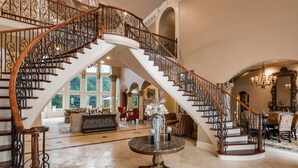 Un intérieur somptueux, avec un escalier imposant, une grande table ronde au centre et un vaste espace de vie offrant de nombreuses possibilités d’assises.