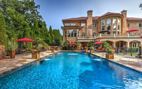 A large swimming pool with a fountain, surrounded by outdoor seating and potted plants.
