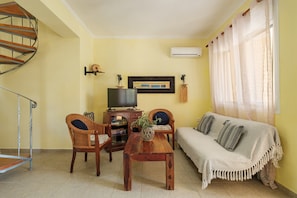 Uma sala de estar com sofá, duas cadeiras, mesa de madeira, televisão e escada.