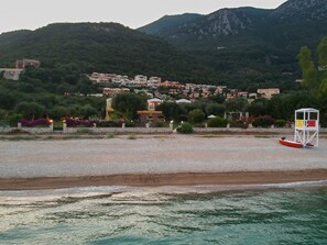 A coastal area with a lifeguard tower, a pebble beach, and a backdrop of residential buildings.