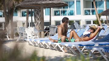 Zona relax in spiaggia con poltrone a righe e ombrelloni di paglia.