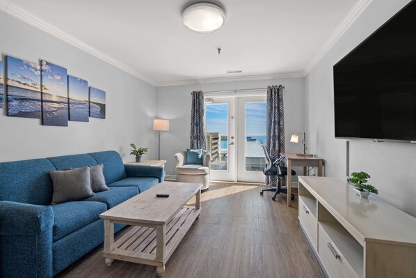Un salon moderne avec un canapé bleu, une table basse en bois, un bureau et un téléviseur.