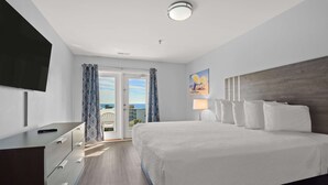 Ein Hotelzimmer mit einem großen Bett, einem Flachbildfernseher, einem Schreibtisch mit Schubladen und Blick ins Freie durch eine Schiebetür.