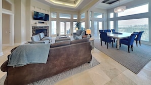 A spacious living room with a brown sofa, a dining area with blue chairs, a fireplace, and large windows.
