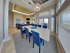 A spacious dining area with a large table, blue upholstered chairs, and a chandelier. - Beach Belle by Distinctive Beach Rentals (Palm Coast)