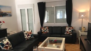 Een woonkamer met een zwarte leren bank, een glazen salontafel en een tv op een meubel.