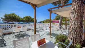 Un espace extérieur aménagé avec des chaises et des tables blanches, une pergola et une enseigne indiquant « Hotel Servigi Group Romana ».