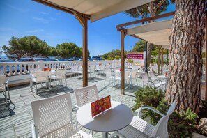 Un espace extérieur aménagé avec des chaises et des tables blanches, une pergola et une enseigne indiquant « Hotel Servigi Group Romana ».